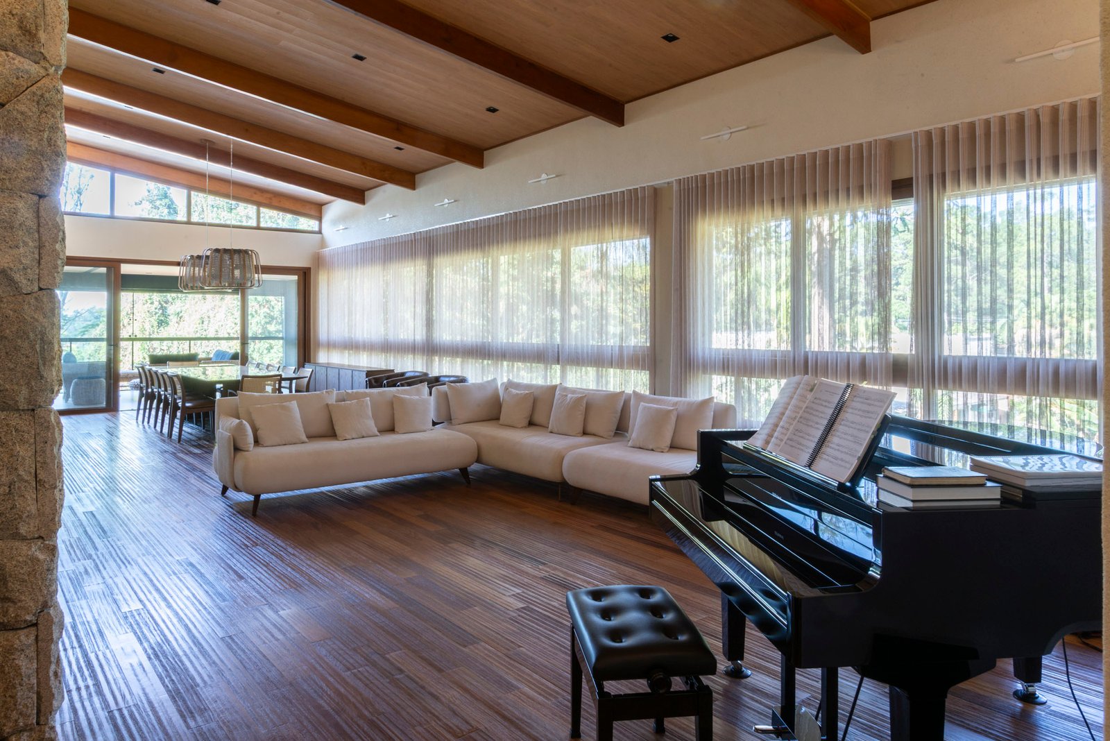 Living da Casa Granja Viana com piano de cauda, cortinas translúcidas e teto em madeira com vigas aparentes